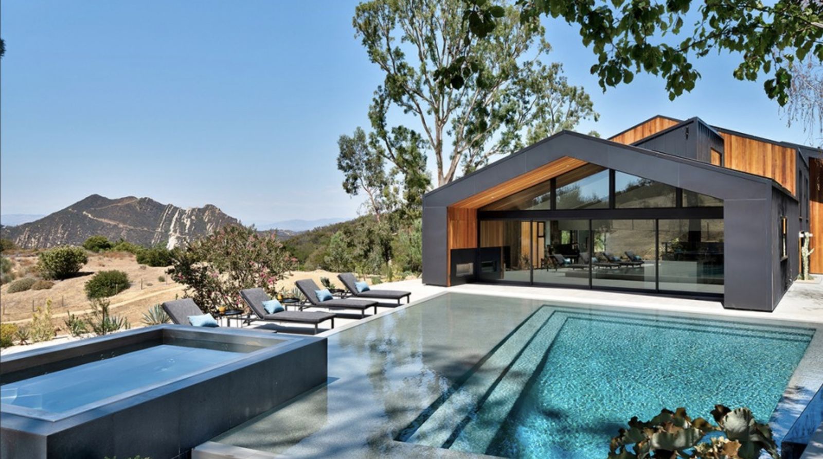 Modern hillside home with a wall of floor-to-ceiling glass beside a pool