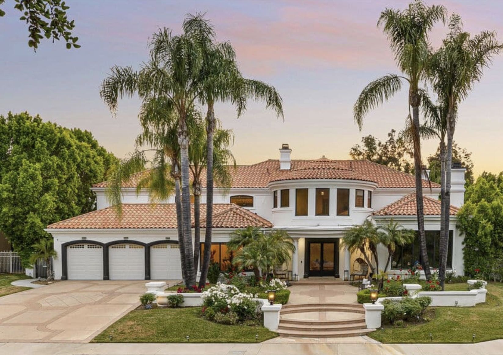 White Spanish-style home with palm trees and sparkling windows at dusk